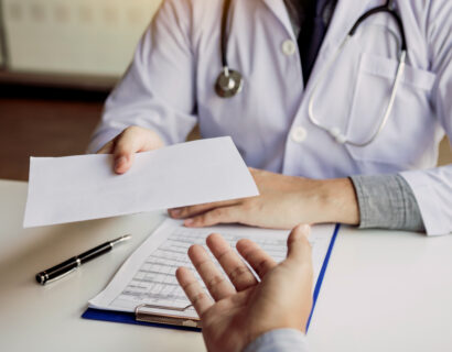 Asian male doctor talking in clinic room and handing a prescription to the patient.